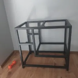 Czarna, metalowa konstrukcja podstawy stolika kawowego z profili zamkniętych, widoczna pomarańczowa zabawka dla psa na podłodze z paneli.