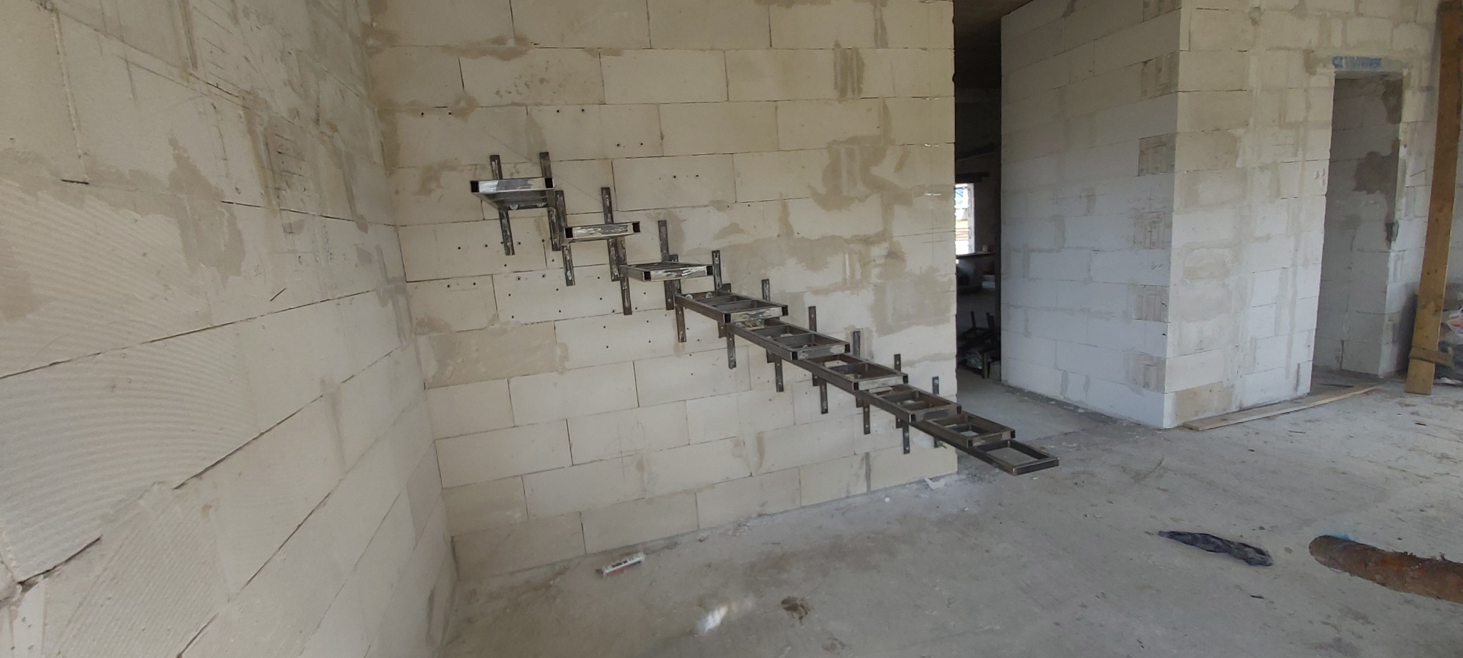 Surowe, metalowe stopnie schodów mocowane do ściany z pustaków w surowym wnętrzu budynku w trakcie budowy.