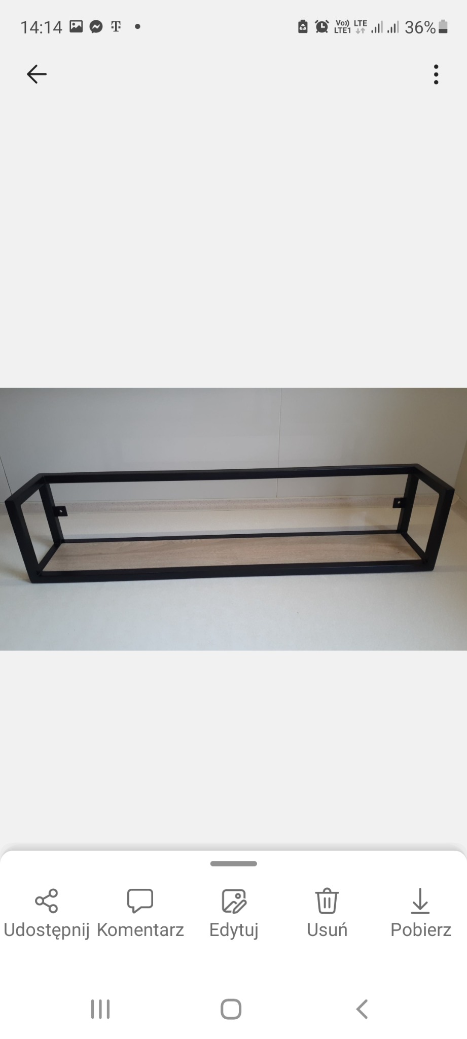 Stelaż metalowy w kolorze czarnym z drewnianą półką, widoczne mocowania do ściany, na jasnym tle.