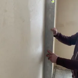 Sprawdzanie pionu ściany po nałożeniu tynku za pomocą poziomicy; widoczna faktura świeżego tynku.