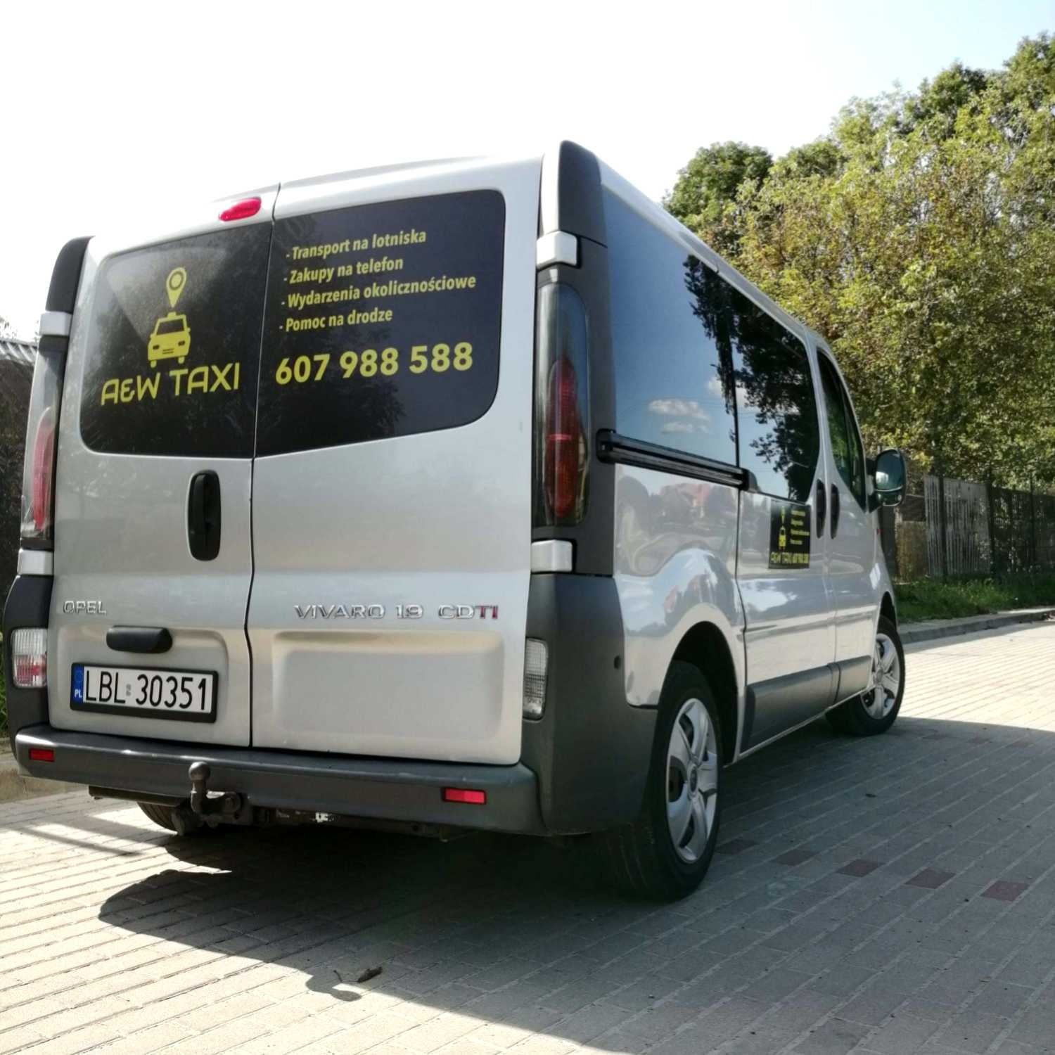 Srebrny bus Opel Vivaro z reklamą usług przewozowych AEW Taxi, widok z tyłu, numer telefonu i zakres usług na tylnej szybie, tablica rejestracyjna LBL 30351.