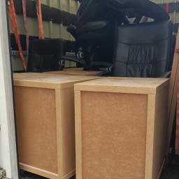 Home Warriors - Dwa biurka z szufladami na kółkach i czarne skórzane krzesło biurowe zabezpieczone pasami wewnątrz furgonetki podczas transportu.