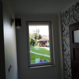 Kompleksowe remonty i elewacje - Wnętrze domu z widokiem na ogród przez okno; na ścianie wzorzysta tapeta i ozdobny kinkiet