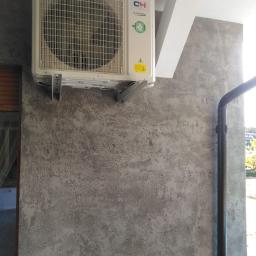 Kompleksowe remonty i elewacje - Zamontowany klimatyzator marki CH Inverter na szarej, teksturowanej ścianie zewnętrznej budynku z widoczną rurą spustową i fragmentem okna.