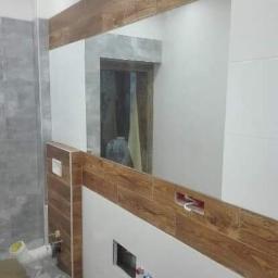 Kompleksowe remonty i elewacje - Fragment łazienki w trakcie wykańczania, z widoczną instalacją hydrauliczną, częściowo ułożonymi płytkami imitującymi drewno oraz przygotowanymi otworami na armaturę.