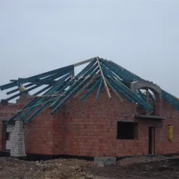 Wznoszenie konstrukcji dachu z drewnianych łat na ceglanym budynku w Rudzie Śląskiej, widoczne elementy więźby dachowej i niezadaszona bryła budynku w stanie surowym.