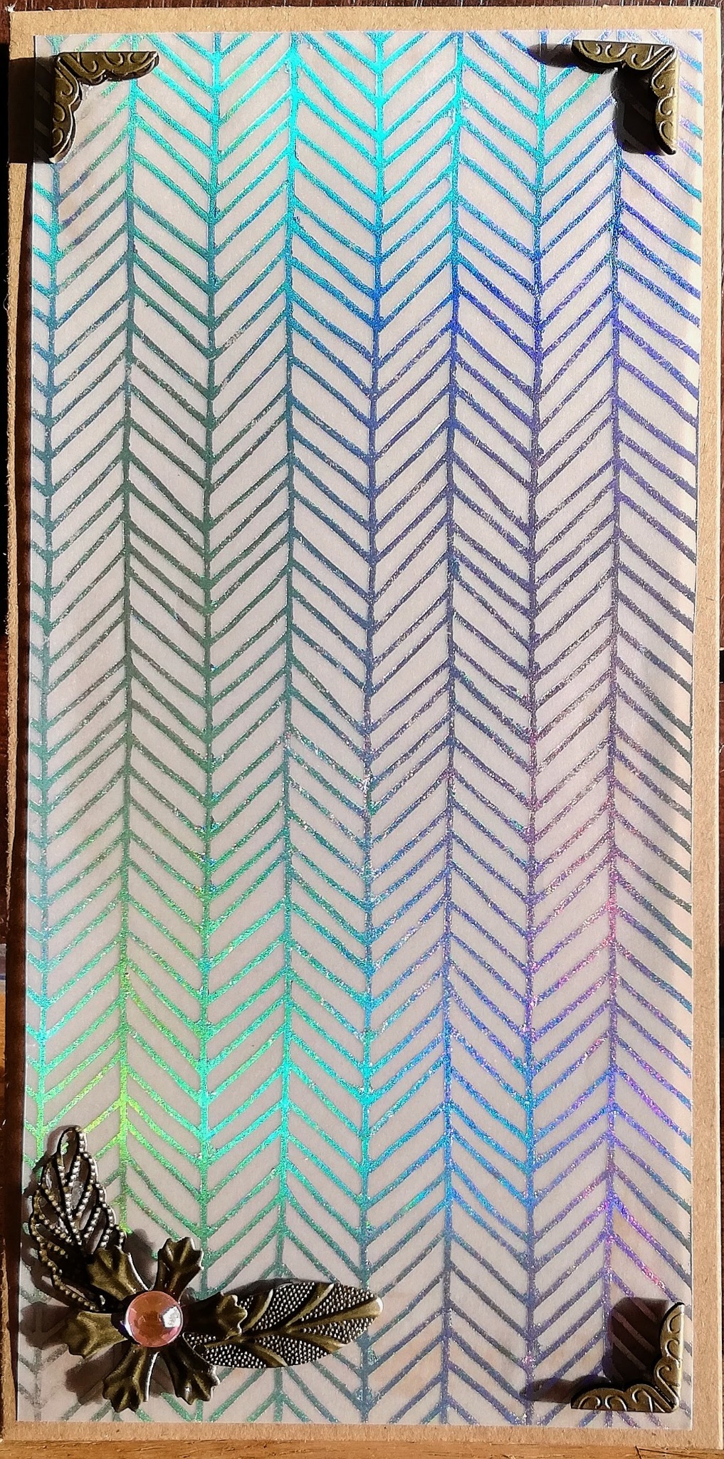 Ręcznie robiona kartka imieninowa z motywem chevron w odcieniach tęczy, ozdobiona metalowymi narożnikami i dekoracją z liści i różowego koralika w stylu scrapbookingu.