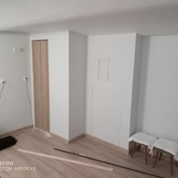 Zakład usługowy Piotr Pionk - Wnętrze pokoju po malowaniu ścian na biało, widoczne dwa stołki z białymi pokrowcami, listwy przypodłogowe i drzwi z jasnego drewna.