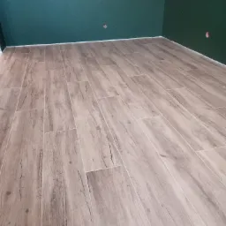 Ukończona podłoga z płytek imitujących drewno w nowo pomalowanym pomieszczeniu z zielonymi ścianami, widoczne puszki elektryczne.