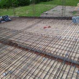 Zakład usługowy Piotr Pionk - Siatka zbrojeniowa na drewnianym szalunku, przygotowana do wylewki betonowej stropu; widoczne dystanse z tworzywa sztucznego i wystające pręty pionowe na obrzeżach.