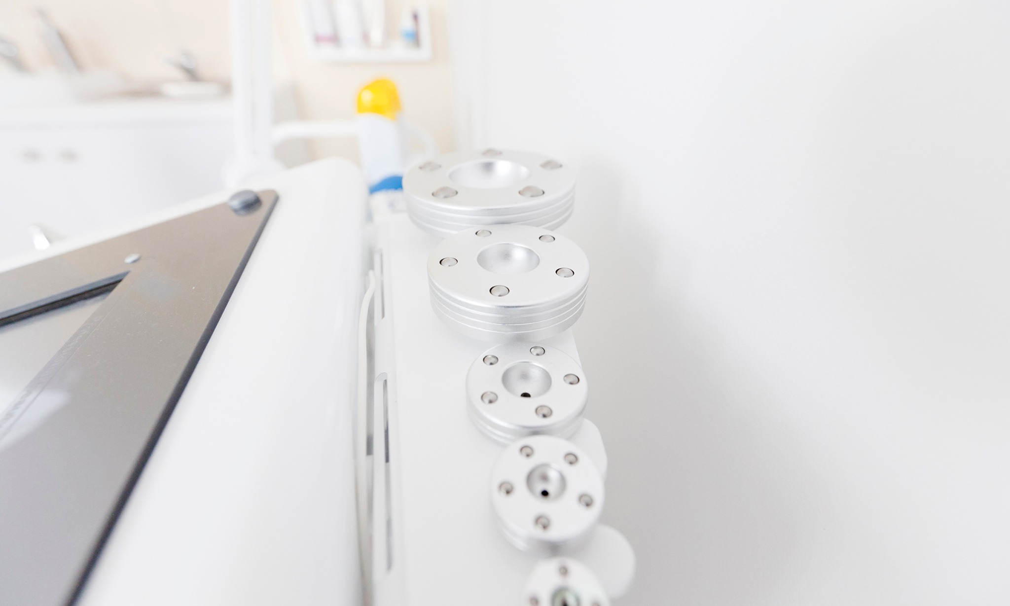 Urządzenie do modelowania sylwetki z wymiennymi, metalowymi głowicami o różnej średnicy, ustawionymi w pionowym rzędzie, na tle białego wnętrza gabinetu.