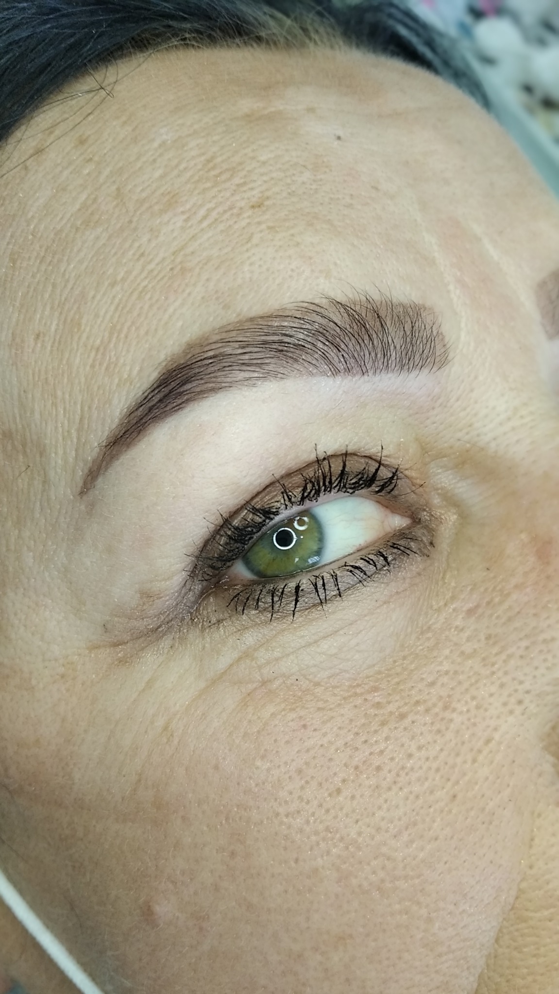 Zbliżenie na oko kobiety z podkreślonymi, świeżo wystylizowanymi brwiami o naturalnym wyglądzie, z widocznymi drobnymi włoskami.