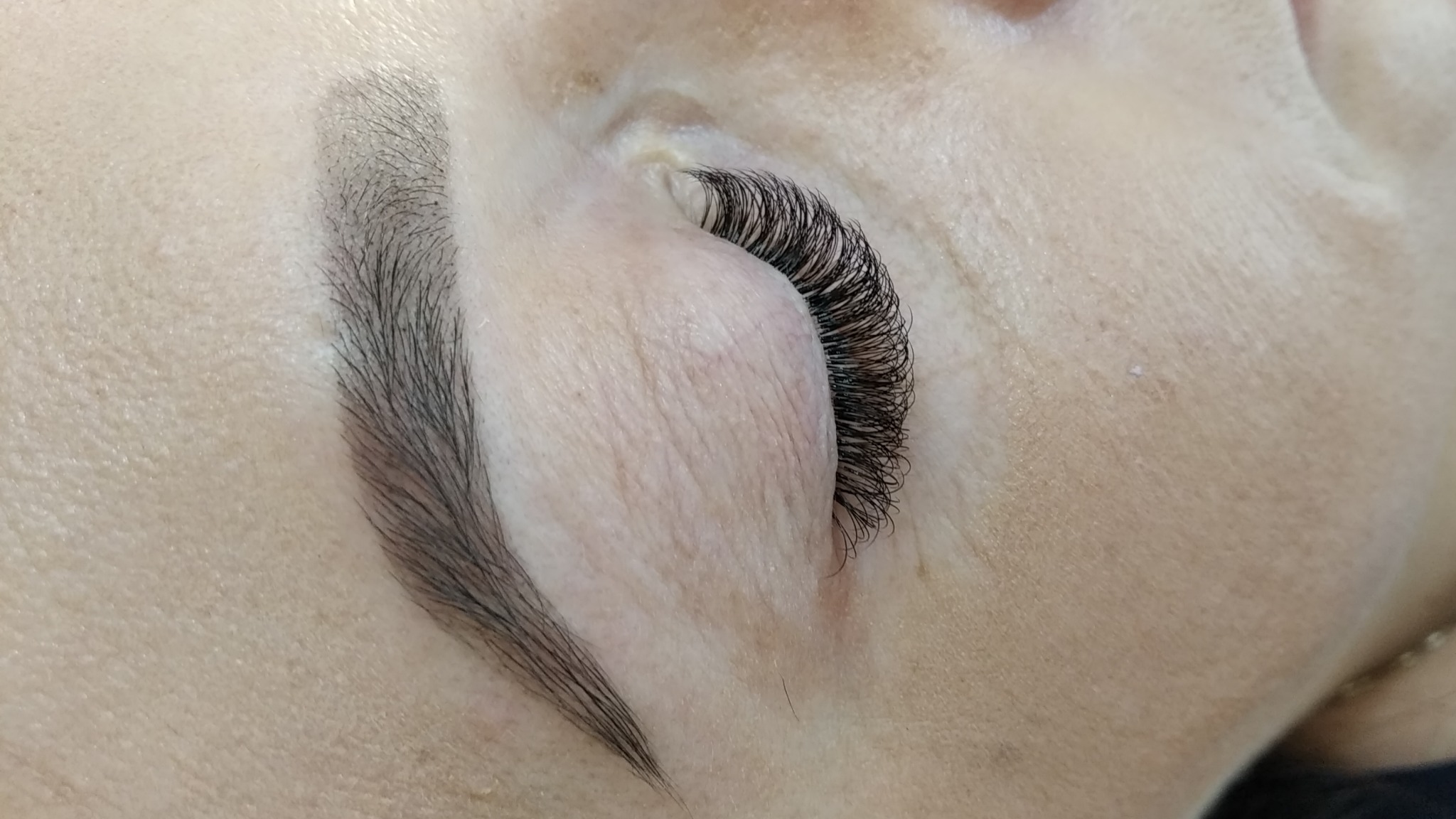Zbliżenie na oko z gęstymi, czarnymi, sztucznymi rzęsami, widoczny również fragment brwi.