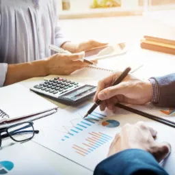 Analiza wykresów finansowych przy biurku z kalkulatorem, notatnikiem i tabletem.