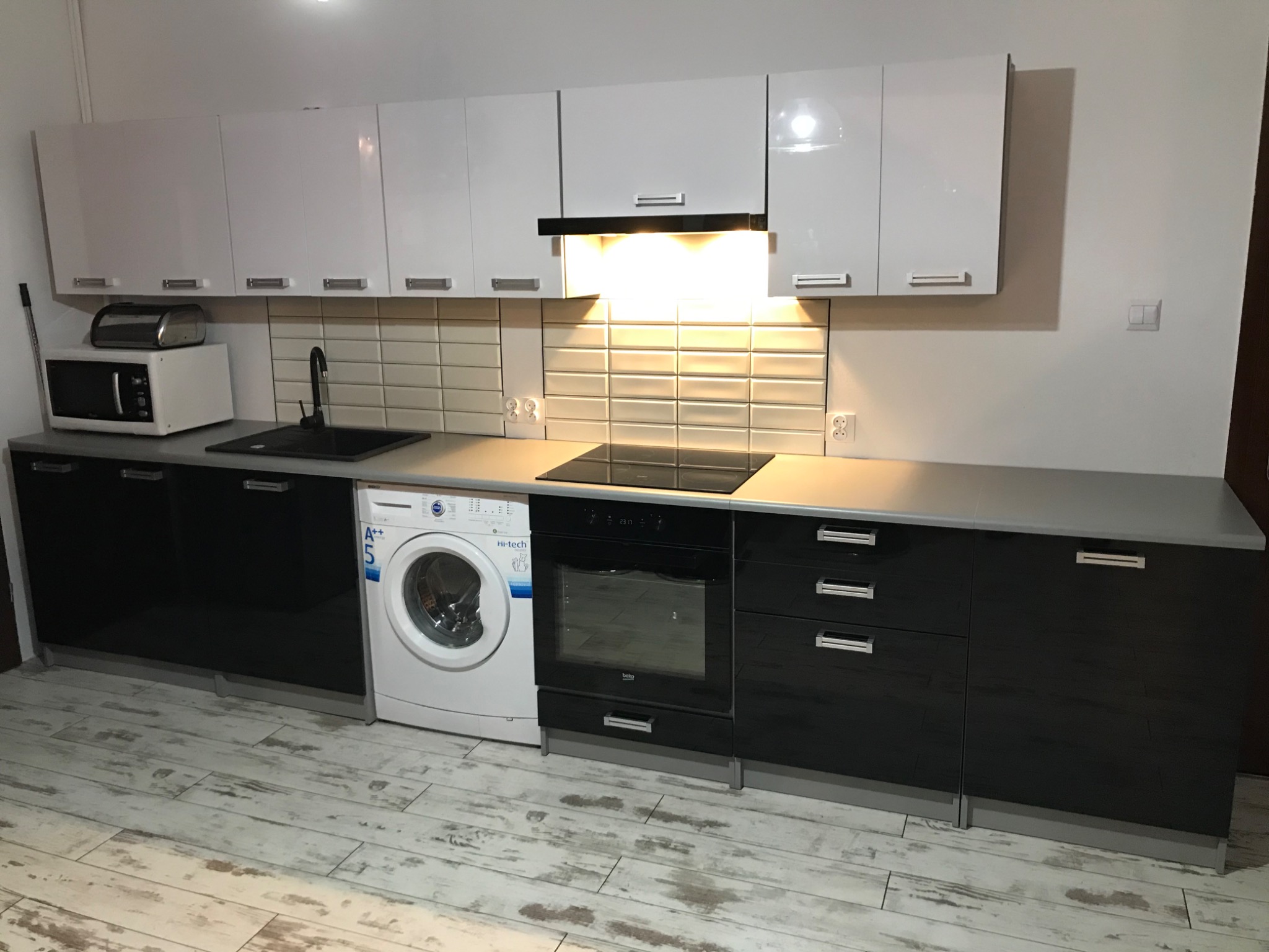 Nowoczesna kuchnia w Żninie z białymi szafkami górnymi i czarnymi dolnymi, z widoczną pralką w zabudowie, płytą indukcyjną i piekarnikiem.