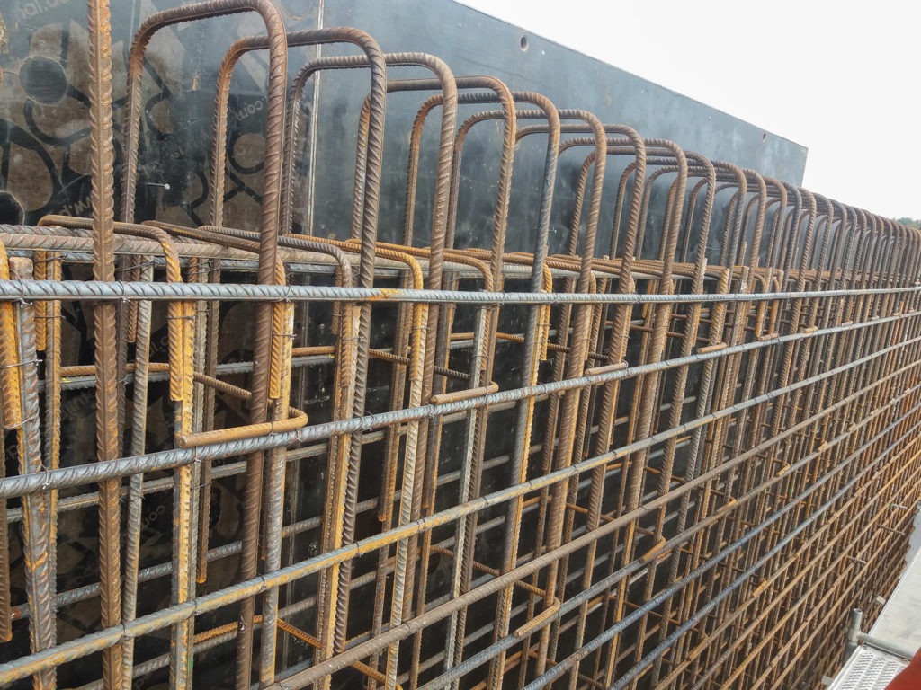 Siatka zbrojeniowa z prętów stalowych, ułożona w regularny wzór, widoczna na tle czarnej szalunku, przygotowana do zalania betonem.