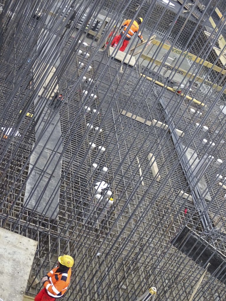Zbrojenie płyty fundamentowej z widocznymi pracownikami w odblaskowych ubraniach, ujęcie z góry.