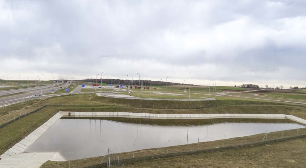 Zbiornik retencyjny z betonowymi brzegami przy nowej drodze ekspresowej, widok z góry w pochmurny dzień.