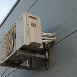 Zewnętrzna jednostka klimatyzacji Mitsubishi Electric zamontowana na szarej ścianie budynku w Orzeszu, widoczne rury i metalowa konstrukcja wsporcza.