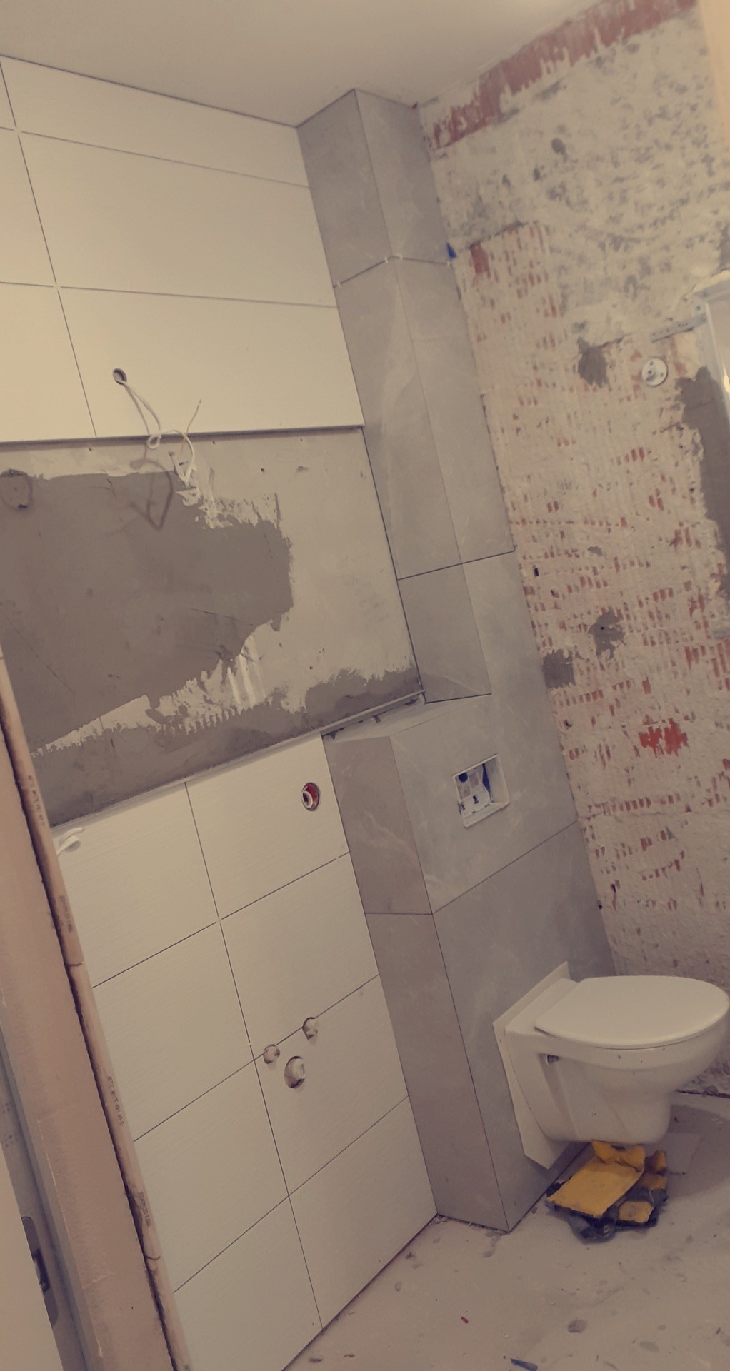 Montaż wiszącej toalety w trakcie kładzenia płytek ściennych w łazience, widoczne surowe ściany i przygotowane otwory na armaturę.