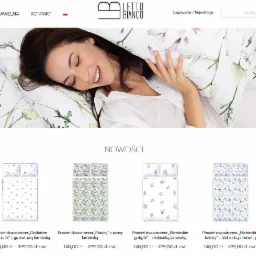 Uśmiechnięta kobieta leżąca na poduszce i kołdrze z delikatnym, akwarelowym motywem kwiatowym w pastelowych odcieniach zieleni i różu, ubrana w białą koszulę.