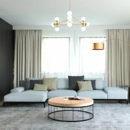 Jasny salon z szarą sofą narożną, okrągłym stolikiem kawowym z metalową podstawą, czarnym regałem z książkami i lampą łukową w kolorze miedzi.