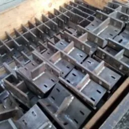 Metalowe, spawane elementy konstrukcyjne w drewnianej skrzyni, widoczne ślady spawania i otwory montażowe.