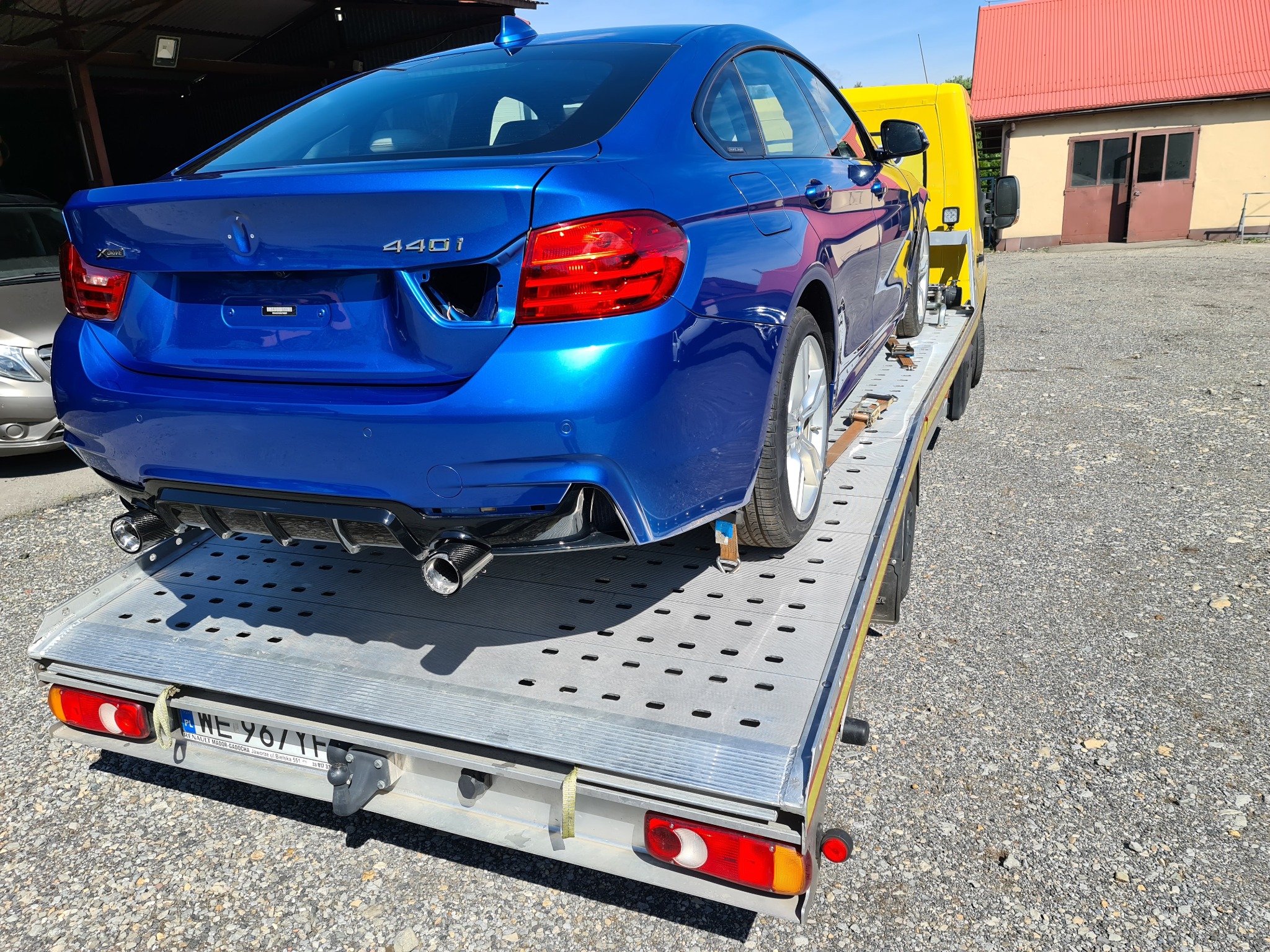 Niebieskie BMW serii 4 (440i) zabezpieczone pasami na żółtej lawecie w Bielsku-Białej, widok z tyłu, z wyraźnie widocznymi końcówkami układu wydechowego i tablicą rejestracyjną lawety.