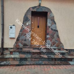 Kamieniarstwo- budowlane i inne usługi - Kamienne schody wejściowe z obudową drzwi z nieregularnych kamieni w odcieniach szarości i czerwieni, prowadzące do drewnianych drzwi wejściowych.