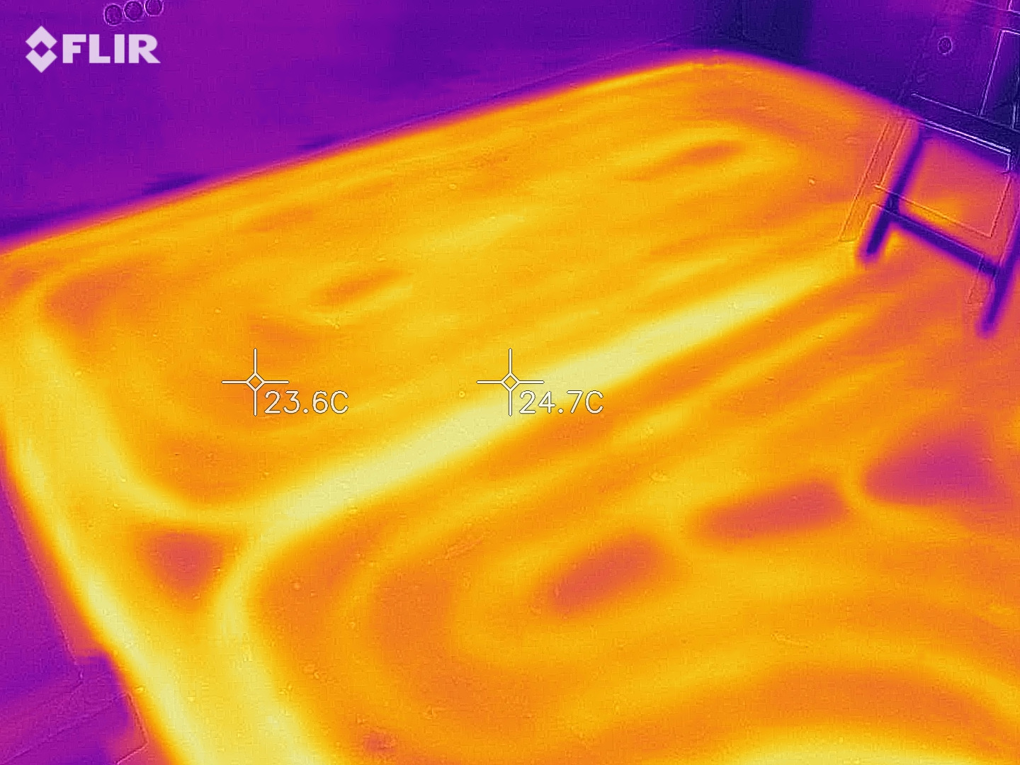 Obraz termowizyjny podłogowego ogrzewania, ukazujący rozkład temperatur w pomieszczeniu, z widocznymi rurami grzewczymi i wartościami temperatury 23.6°C i 24.7°C, wykonany kamerą FLIR.