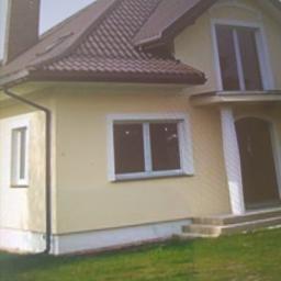 Godeltin - Żółta elewacja domu jednorodzinnego z brązowym dachem, widoczne okna z białymi ramami i kolumny przy wejściu.