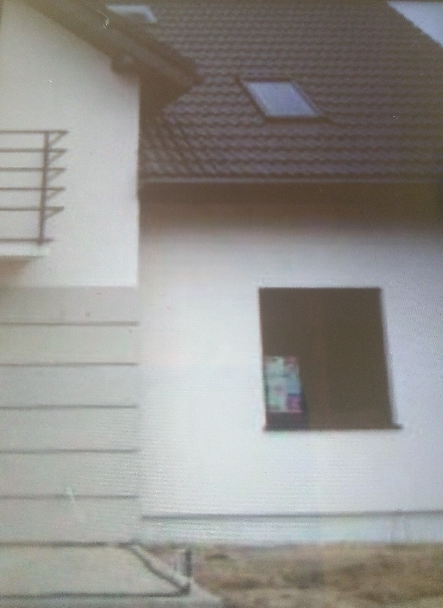 Świeżo otynkowana elewacja domu jednorodzinnego w Gdańsku, z widocznym oknem i fragmentem dachu pokrytego brązową dachówką.