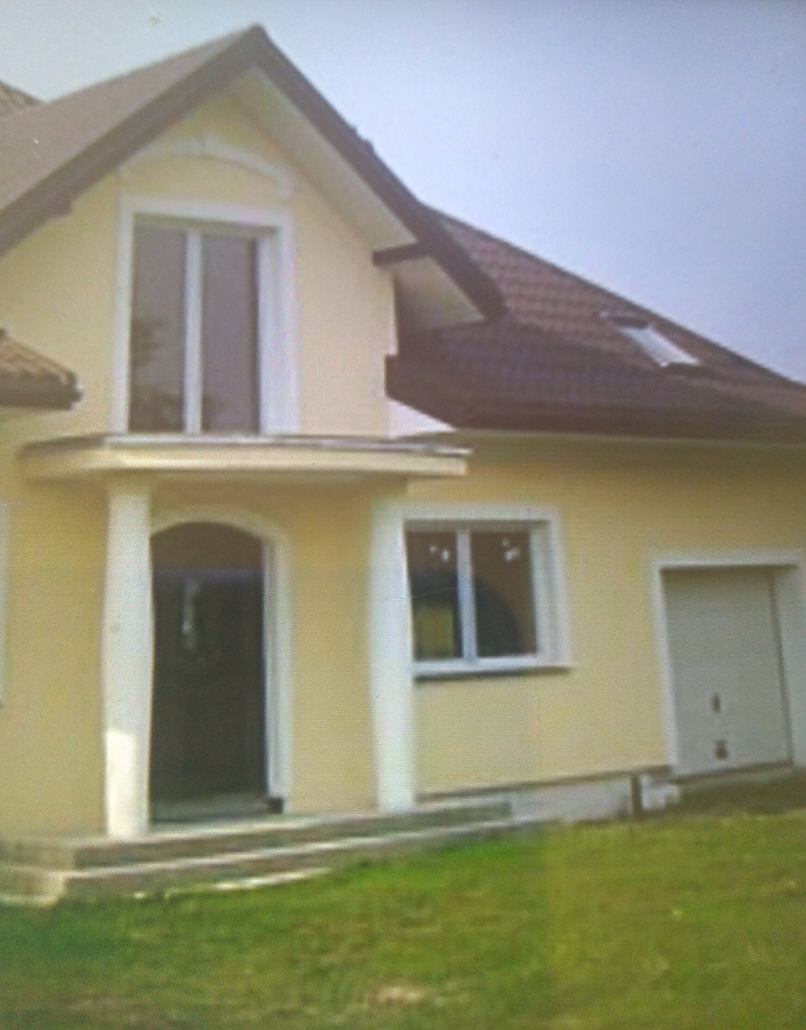 Żółty dom jednorodzinny z brązowym dachem, widoczne okna z białymi ramami, drzwi wejściowe z kolumnami i garaż z bramą segmentową.