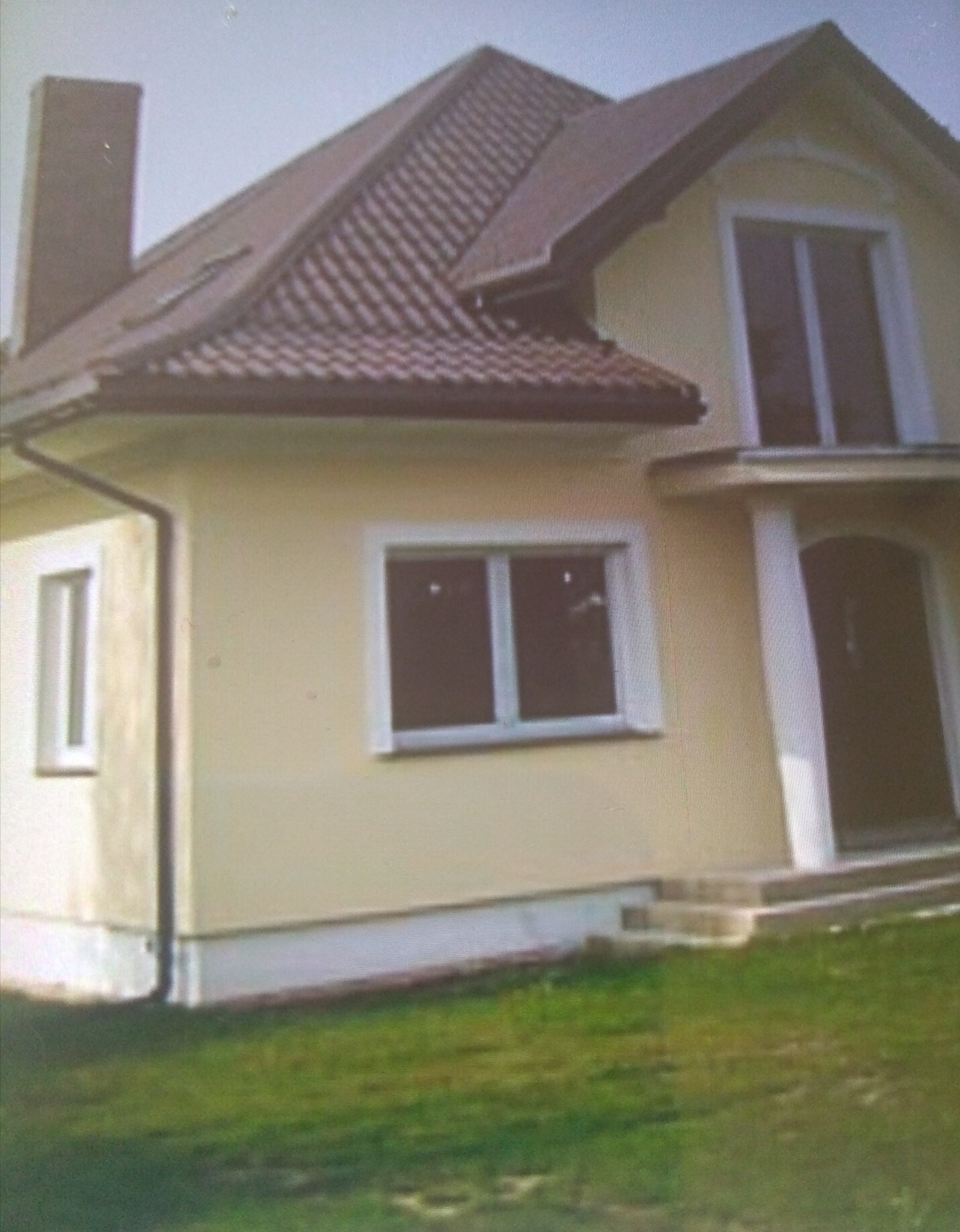 Żółta elewacja domu jednorodzinnego z brązowym dachem, widoczne okna z białymi ramami i kolumny przy wejściu.