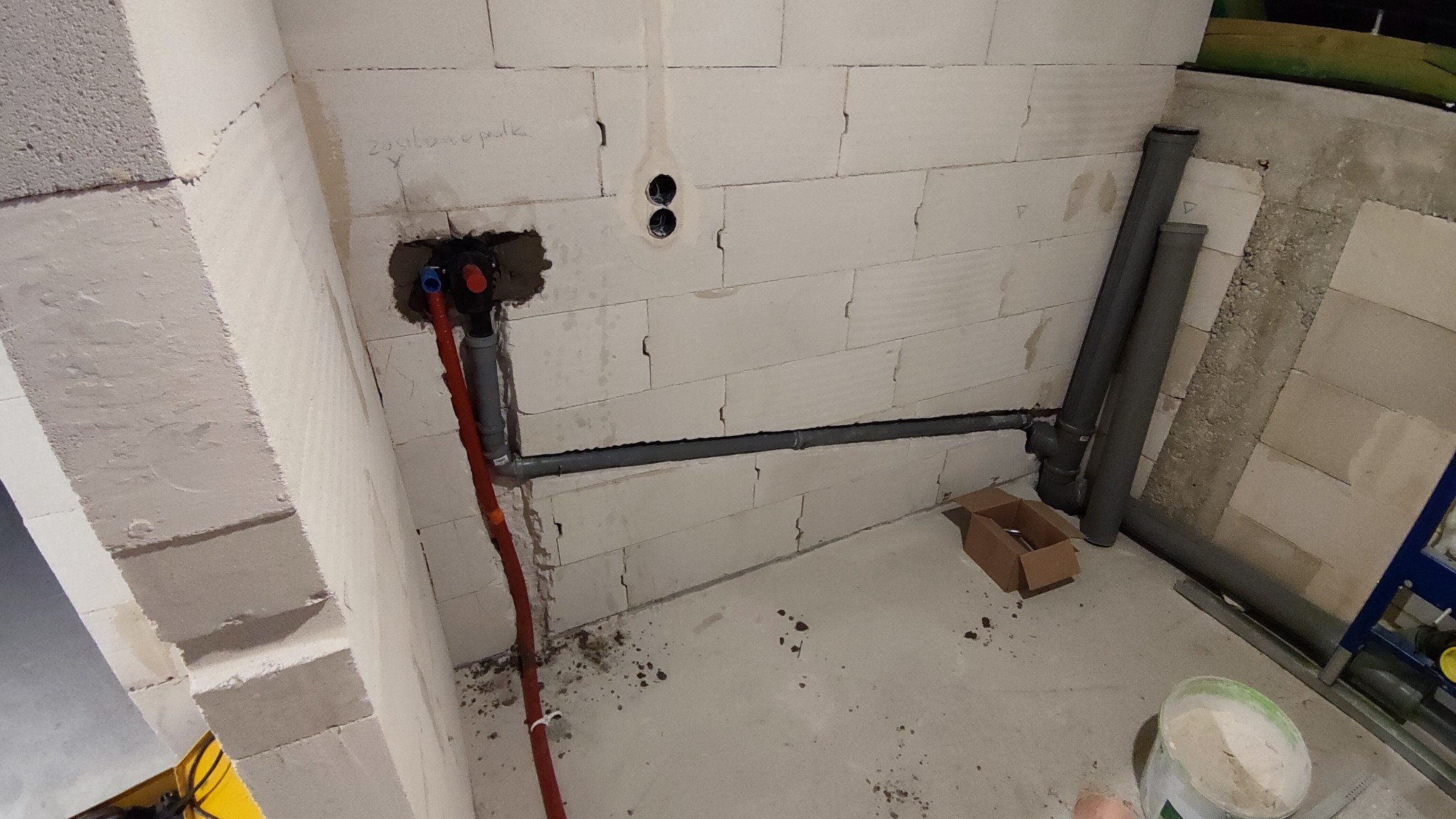 Wewnętrzna instalacja hydrauliczna w trakcie montażu: widoczne rury z tworzywa sztucznego, zawór podtynkowy, ściany z betonu komórkowego i fragment podłogi z drobnymi zabrudzeniami.