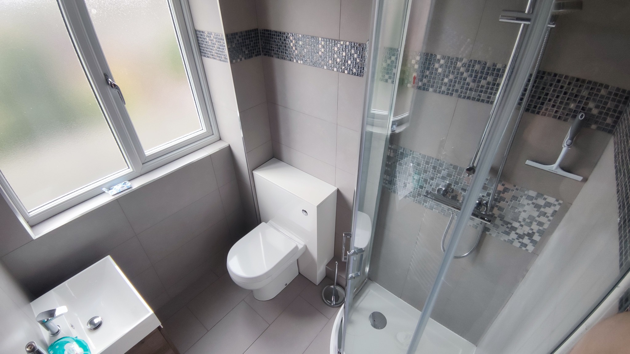 Nowoczesna, szaro-biała łazienka z kabiną prysznicową, umywalką i toaletą w zabudowie, wykończona mozaiką dekoracyjną, widok z góry.