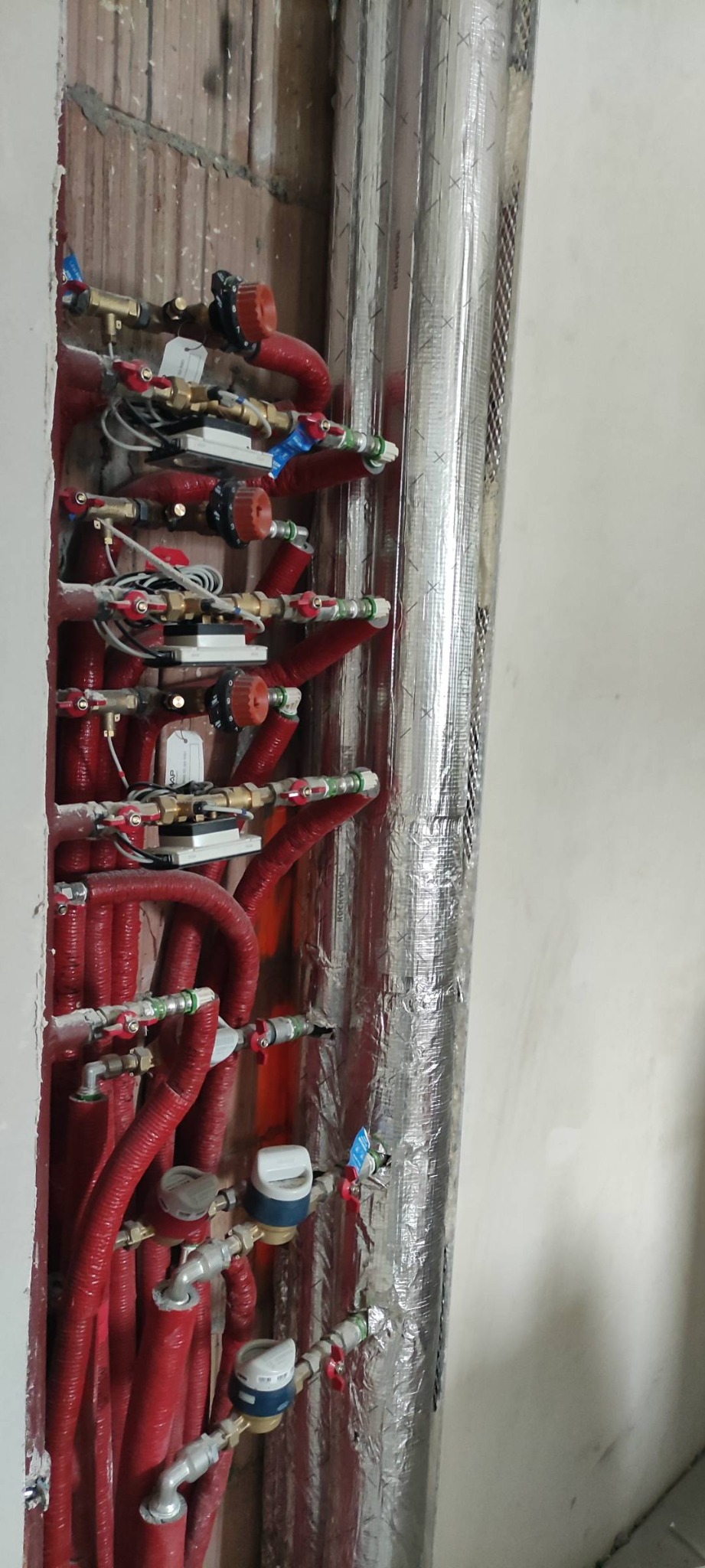 Rozdzielacz ogrzewania podłogowego z rurami w izolacji termicznej, zamontowany w ścianie w trakcie prac instalacyjnych.