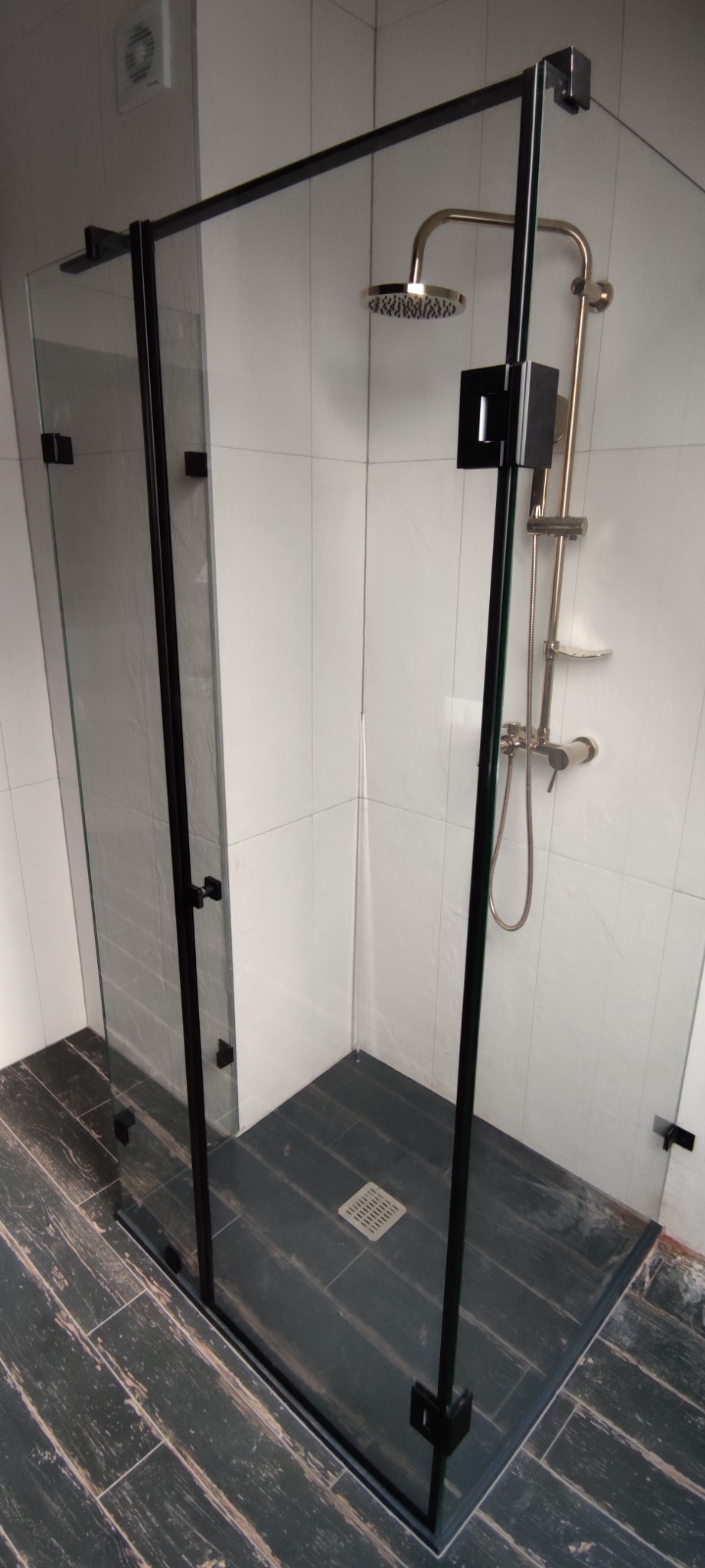 Nowoczesna kabina prysznicowa z czarnymi profilami i deszczownicą, wykończona płytkami imitującymi drewno.