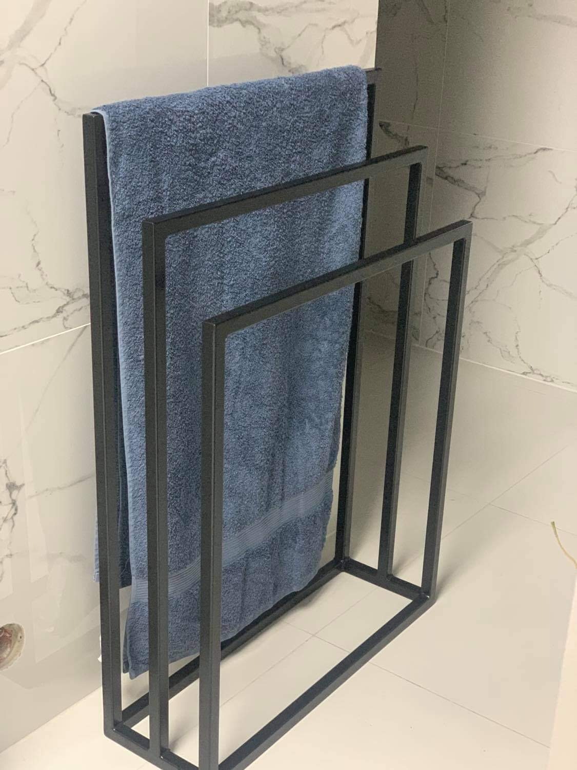 Minimalistyczny, metalowy stojak na ręczniki w łazience z marmurowymi płytkami, eksponujący niebieski ręcznik.