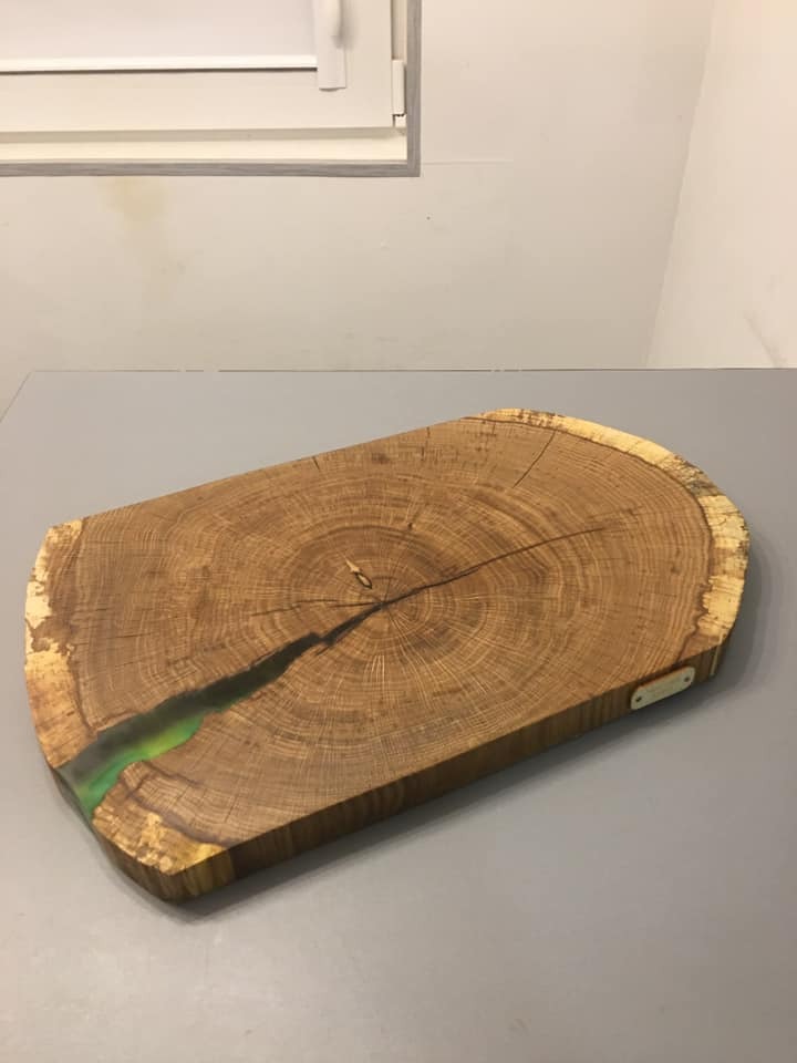 Drewniany plaster z widocznymi słojami, wypełniony zieloną żywicą epoksydową, leżący na szarym blacie.