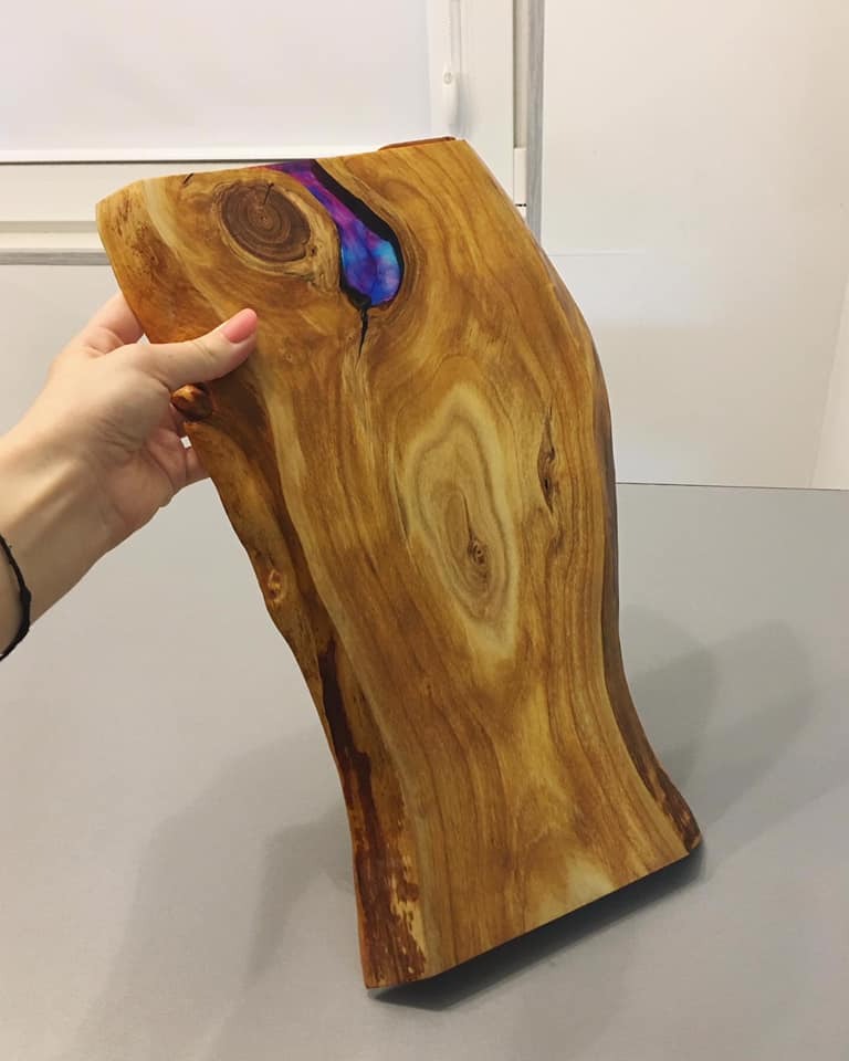 Kawałek drewna z żywicą epoksydową w odcieniach fioletu i niebieskiego, trzymany w dłoni, ukazujący unikalny wzór słojów drewna.