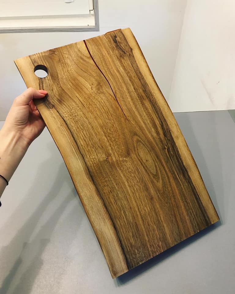 Deska do krojenia z litego drewna z naturalnym pęknięciem, trzymana w ręce, z otworem do zawieszenia.