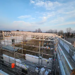 Wysoki kąt: budowa domu z białych bloczków, rusztowania, stalowa konstrukcja dachu na tle błękitnego nieba o zmierzchu. Widok z góry na plac budowy.