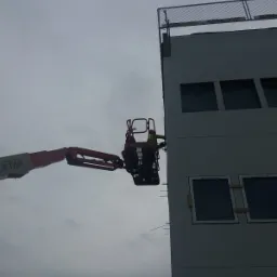 Pracownik w podnośniku koszowym montuje płyty elewacyjne na budynku, widoczne okna zabezpieczone folią.