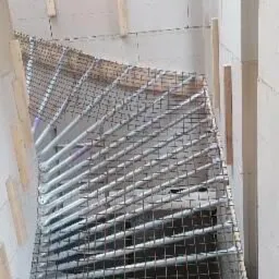 Siatka zbrojeniowa ułożona w drewnianej ramie, przygotowana do zalania betonem w przestrzeni między ścianami z białych bloczków, widoczne drewniane podpory.