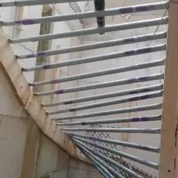 Metalowe rurki w drewnianej konstrukcji poddasza, przygotowane do izolacji, widoczne także bloczki betonowe ścian.