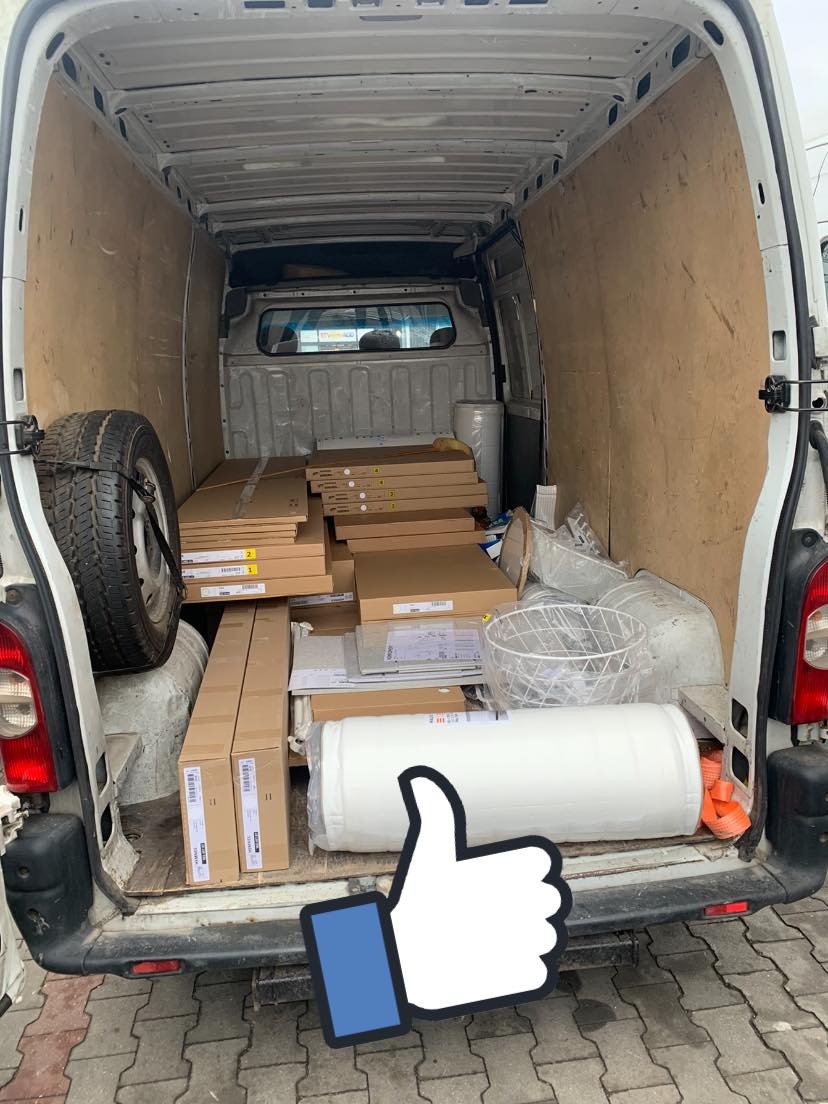 Wnętrze brudnego busa z zapakowanymi elementami mebli w kartonach, zwiniętym materacem i zapasowym kołem, przygotowanymi do przewozu.