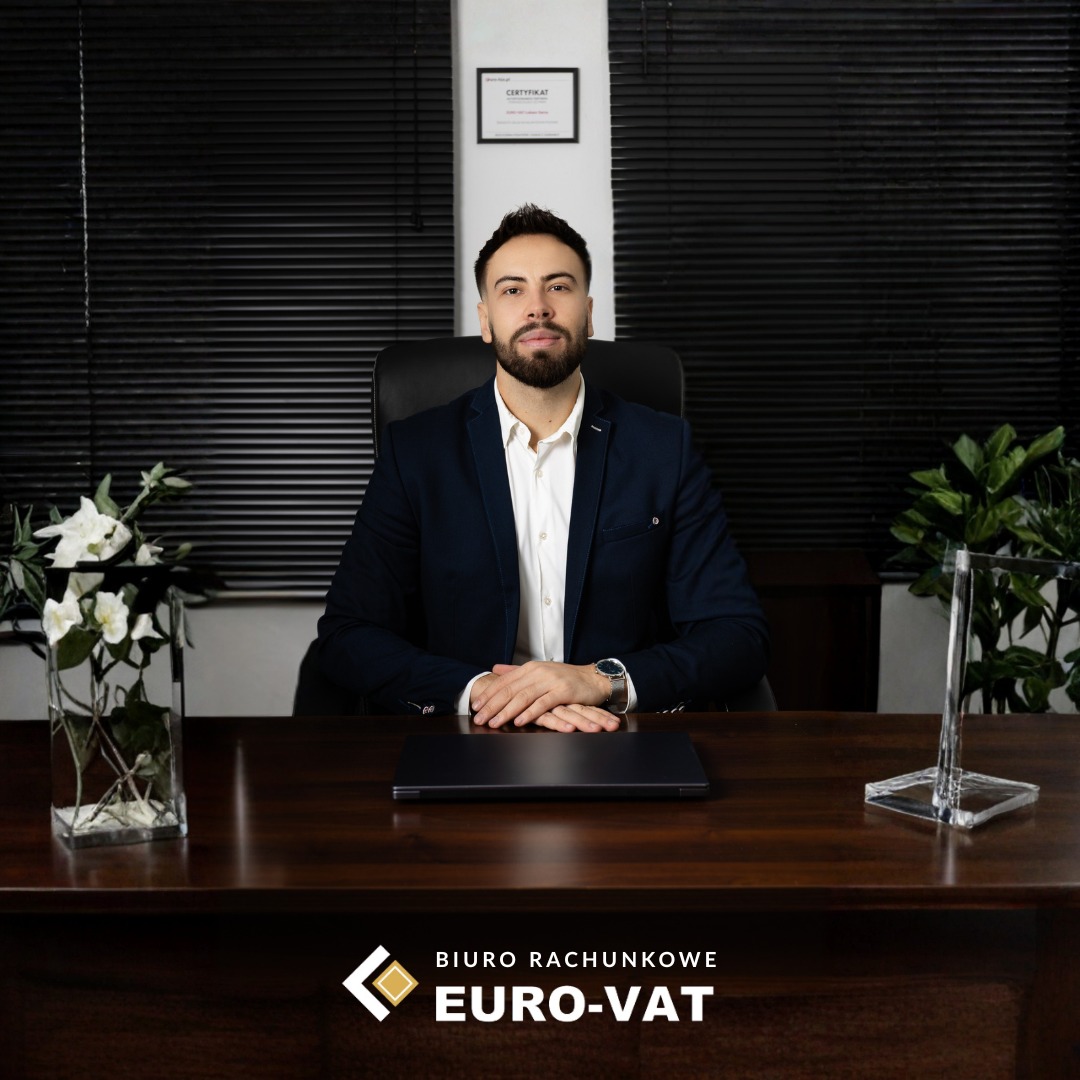 Portret mężczyzny w garniturze siedzącego za biurkiem z laptopem i dekoracjami roślinnymi, w tle żaluzje i certyfikat. Reprezentacja biura rachunkowego.