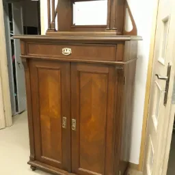 Antyczna, dwudrzwiowa szafa z szufladą i nadstawką z kolumnami oraz lustrem, wykonana z ciemnego drewna z widocznym usłojeniem.