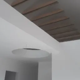 Wnętrze w trakcie wykańczania: surowy strop z drewnianymi belkami, gładkie, białe ściany i okrągły otwór w suficie na oświetlenie.